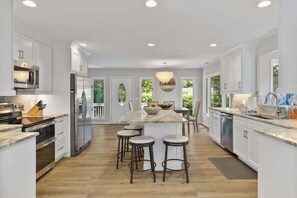 Une cuisine moderne avec des meubles blancs, des appareils en acier inoxydable, un îlot en marbre avec des tabourets et un lustre.
