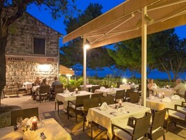 Un espacio de comedor al aire libre con muros de piedra y mesas preparadas para la cena, con vistas a un cuerpo de agua.