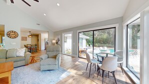Uma sala de estar espaçosa com uma grande porta de vidro deslizante que dá para uma área de piscina externa.