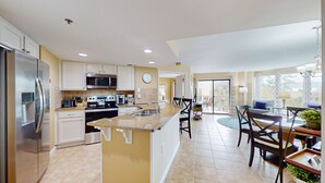 A modern kitchen with a central island, stainless steel appliances, and a dining area with a view to the outdoors. - Comfortable Two Bedroom Villamare Condominium in Palmetto Dunes! (Hilton Head)