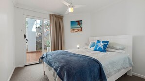 A bedroom with a bed, a ceiling fan, a nightstand, a painting, and a view of a staircase.