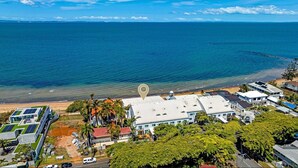 An aerial view of a coastal property with a large building, a beach, and a clear view of the ocean.