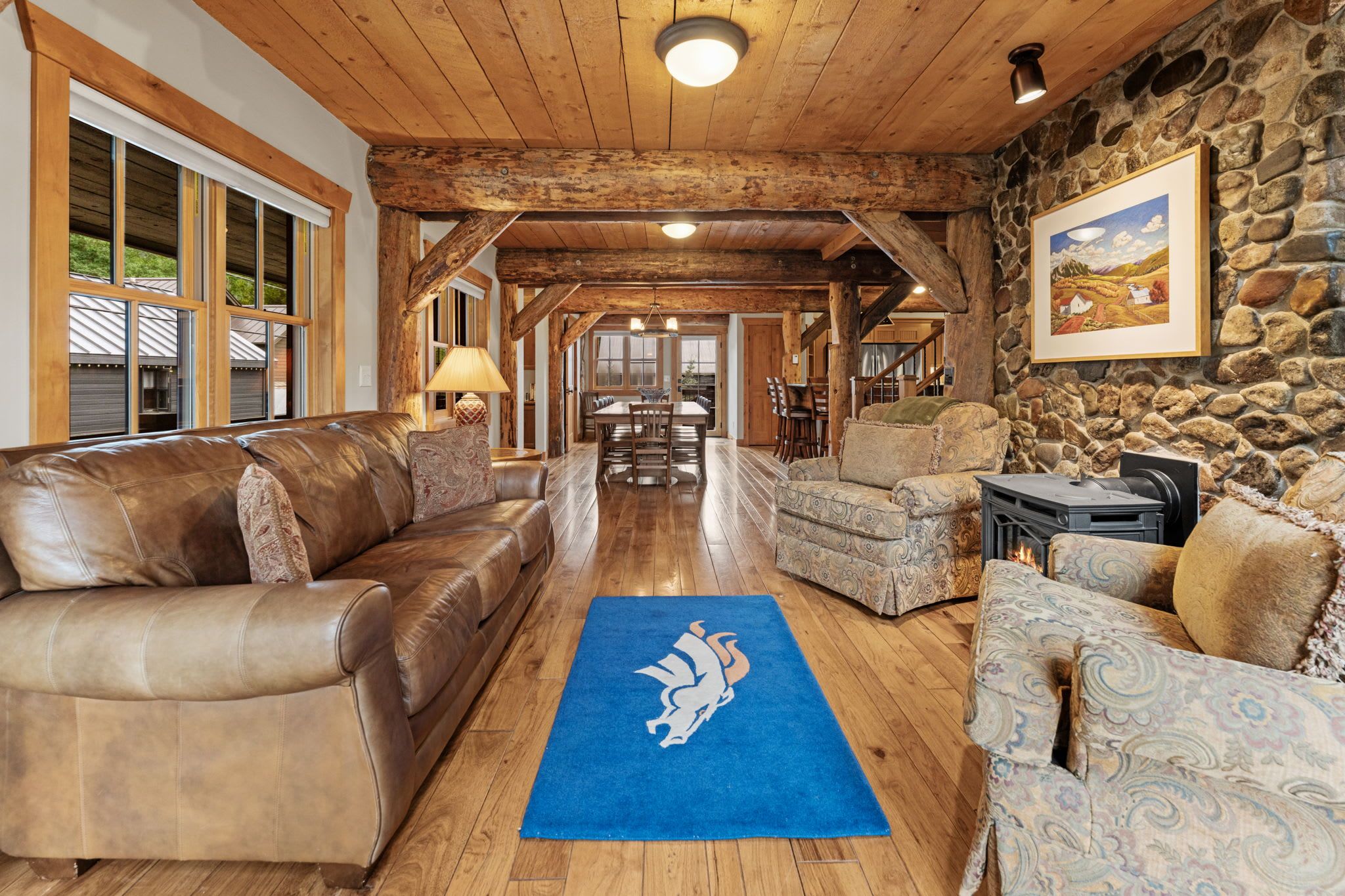 A spacious living area with a stone wall, leather sofas, and a blue rug with a horse logo.