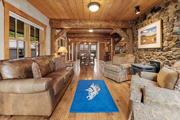 A spacious living area with a stone wall, leather sofas, and a blue rug with a horse logo.
