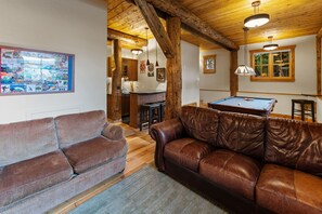 A cozy living room with a pool table, leather sofas, wooden beams, and a bar area.
