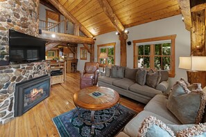 A cozy interior with a stone fireplace, wooden ceiling beams, a leather sofa, and a dining area.