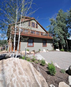 A two-story house with a balcony, surrounded by large rocks and trees.