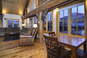 A log cabin interior with a wooden dining table, leather chairs, a sofa, and large windows offering mountain views. - Totem House (Crested Butte)