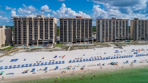 A beachfront hotel with multiple high-rise buildings, a sandy beach with umbrellas and sun loungers, and a clear blue sky.