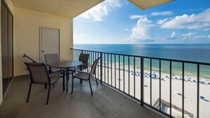 A balcony with a table and chairs, overlooking a beach with umbrellas.
