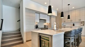 Uma cozinha moderna com uma ilha central, banquetas e iluminação pendente.