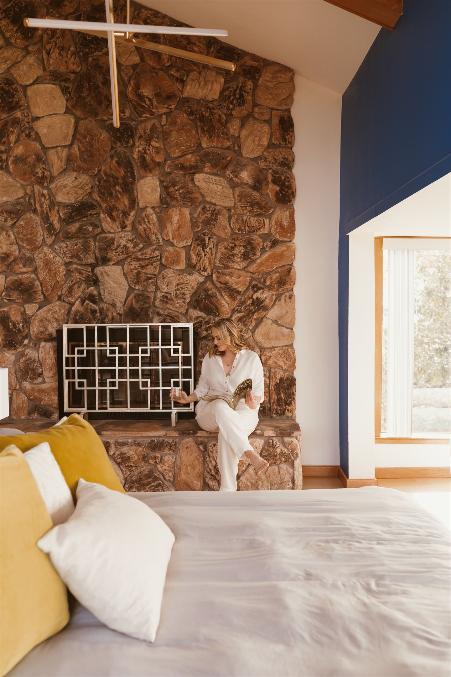 Un dormitorio con pared de piedra, un ventanal grande y una cama con almohadas.
