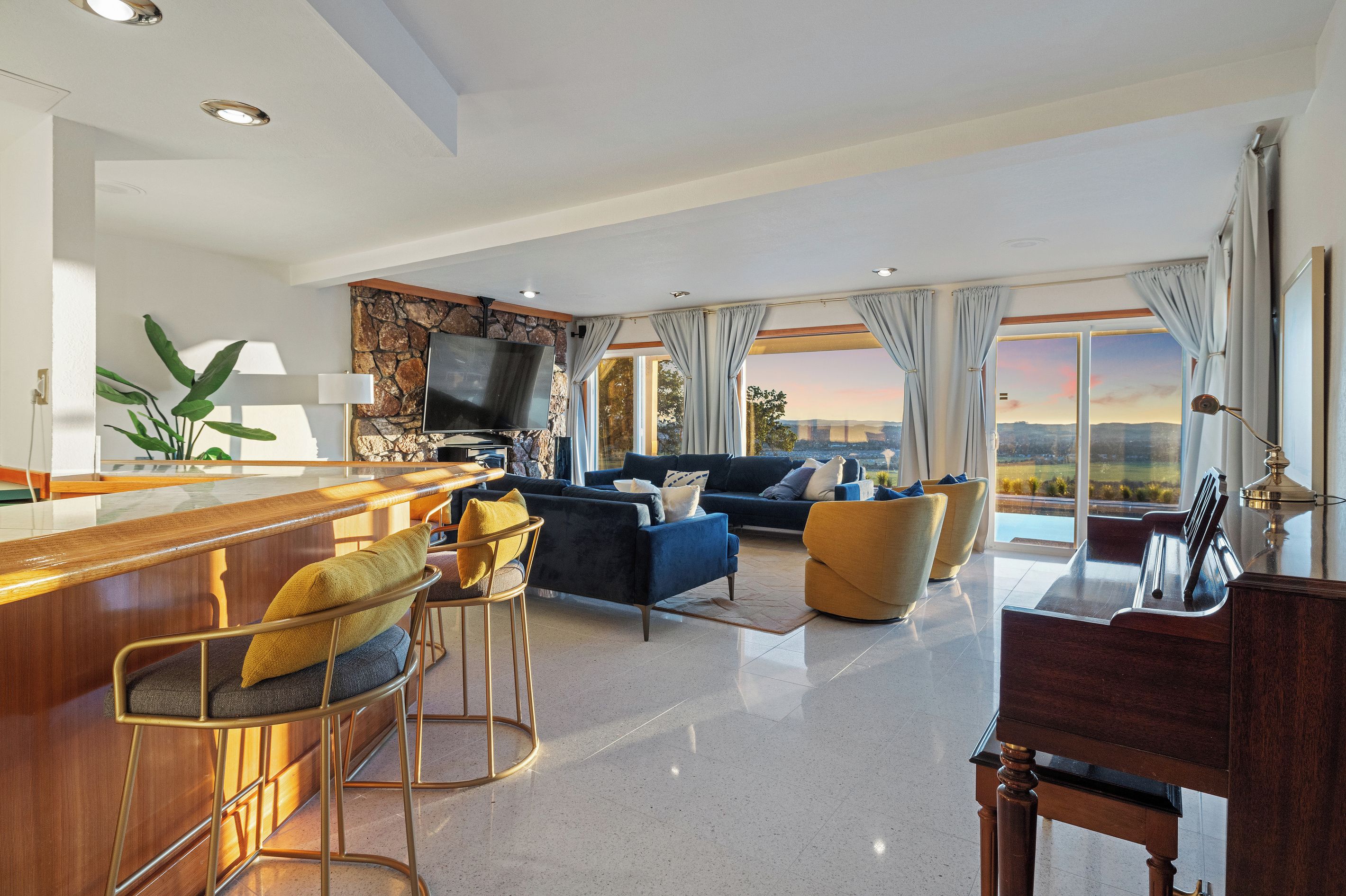 A modern living room with a bar area, seating, a flat-screen TV, and a view of the cityscape.