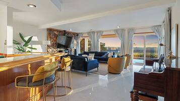 A modern living room with a bar area, seating, a flat-screen TV, and a view of the cityscape.