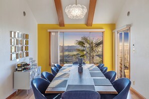 A dining room with a long table, blue chairs, and a view of a landscape through large windows.