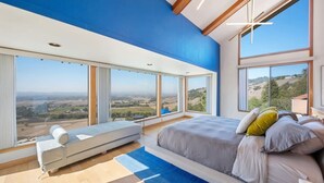 Une chambre dotée d’un grand lit, d’un coin salon et de grandes fenêtres donnant sur la campagne.