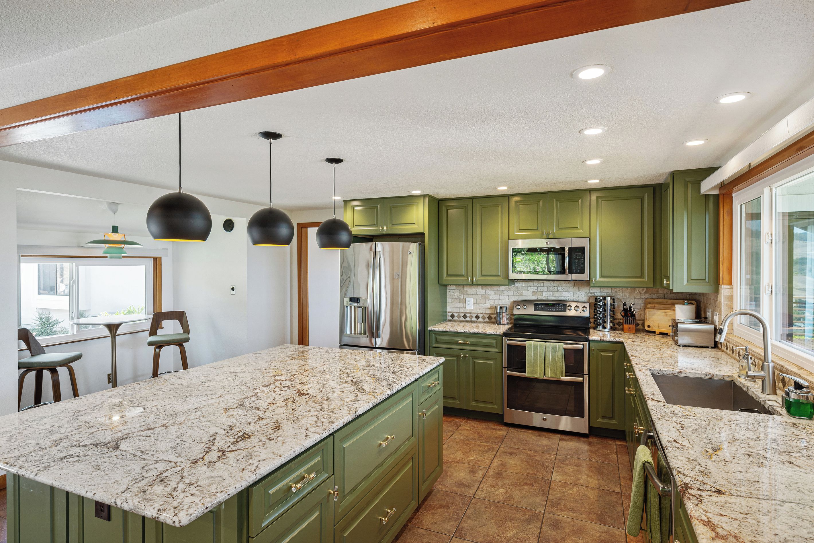 A kitchen with green cabinets, a large island, stainless steel appliances, and pendant lighting.