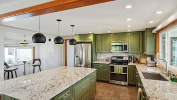 A kitchen with green cabinets, a large island, stainless steel appliances, and pendant lighting.