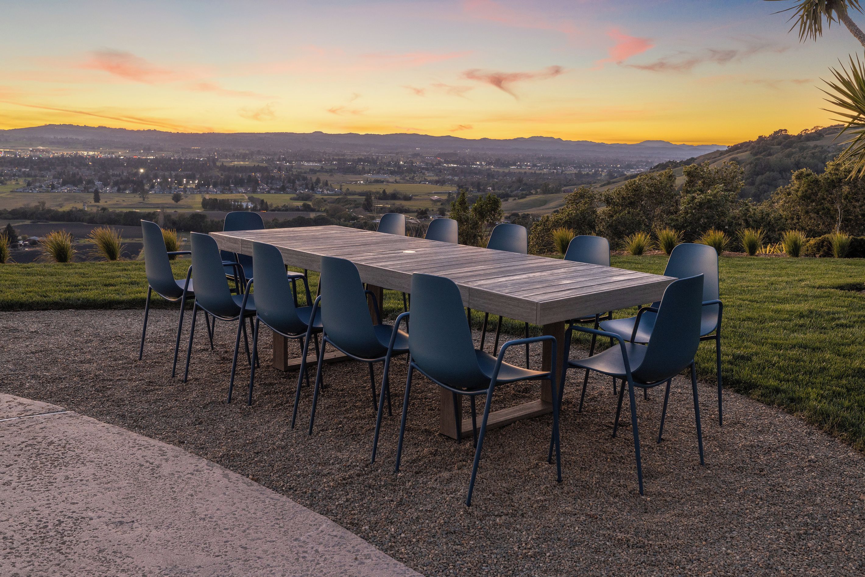 An outdoor dining area with a table and chairs, set on a gravel surface with a view of a distant landscape.
