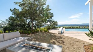 Un patio extérieur moderne avec un foyer, un canapé blanc et une piscine en arrière-plan.