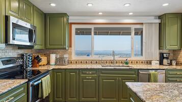 Una cocina con armarios verdes, microondas, estufa, ventana con vistas y cafetera.