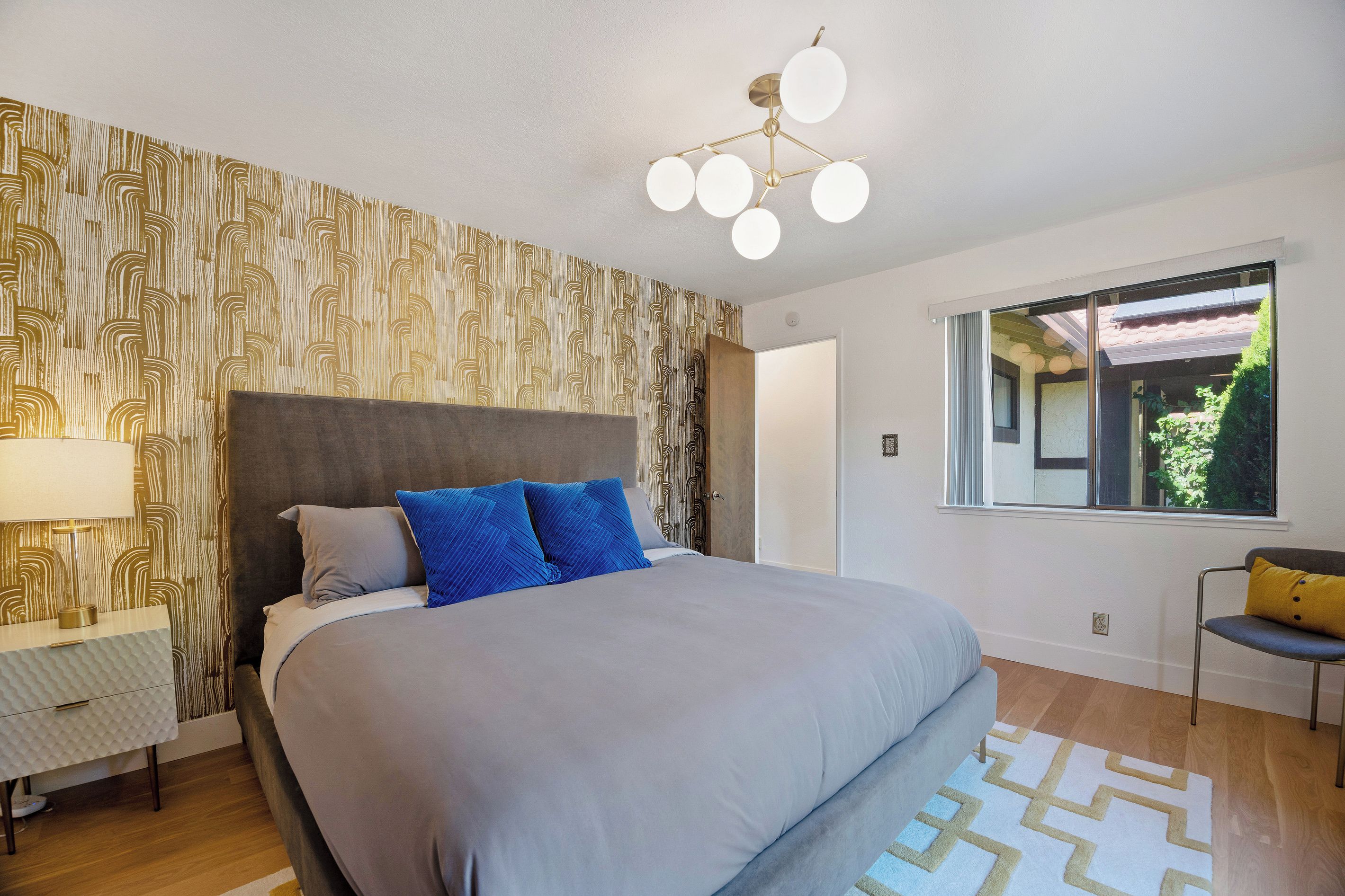 Een slaapkamer met een groot bed, een nachtkastje, een lamp, een raam met uitzicht en een modern plafondlamp.