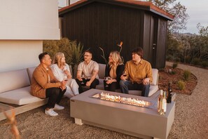 A group of people seated on a white sofa with a modern outdoor fire feature in front. - Sky View: Heated Pool & Hot Tub, 5 Acres (Santa Rosa)