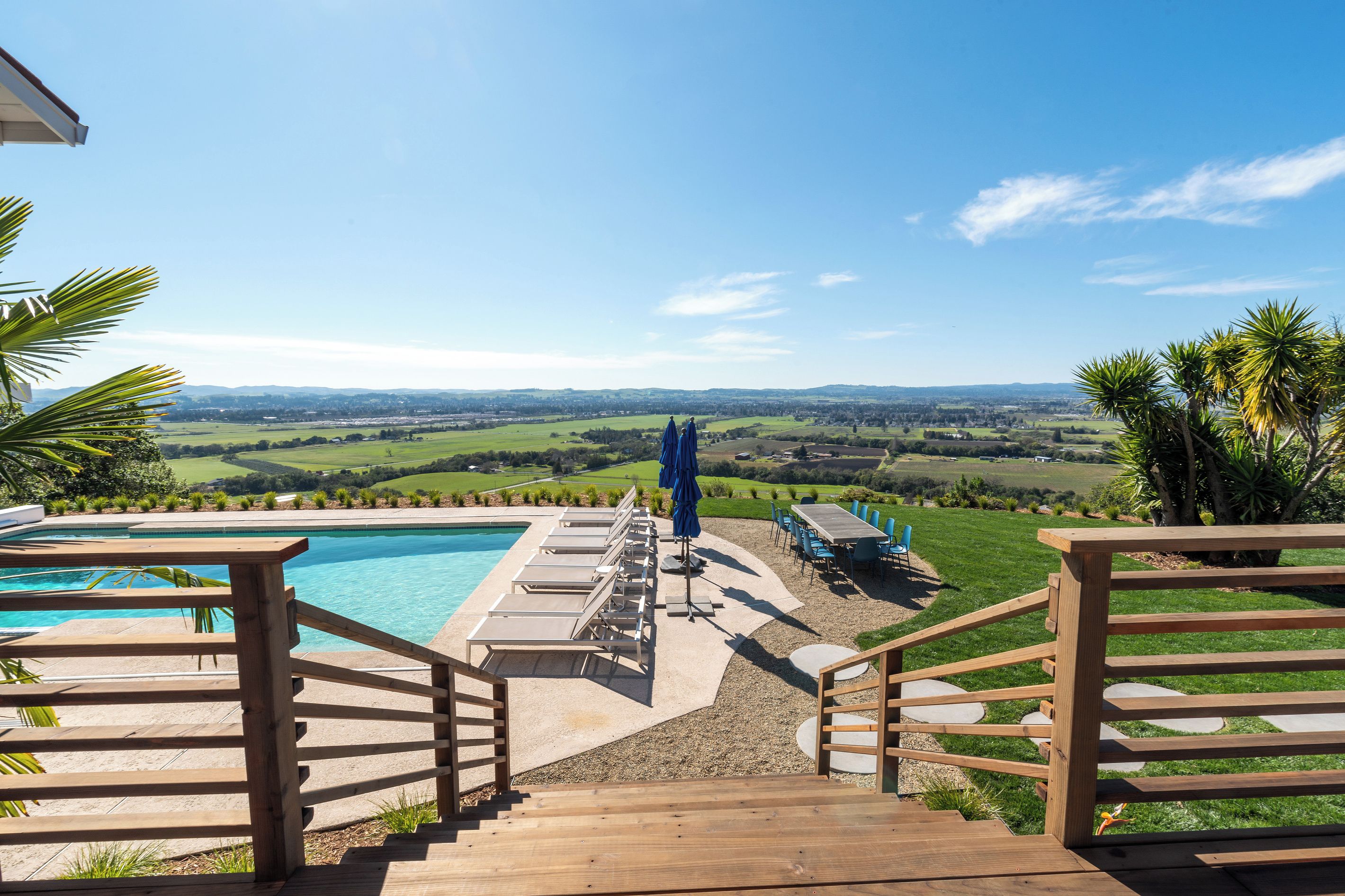 A wooden deck leading to a pool with a view of a green landscape.