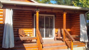 A wooden cabin with a porch, two chairs, a table, and a sliding glass door. - Dry Creek Ranch ~ Pool, HotTub, & Game Barn! (Healdsburg)