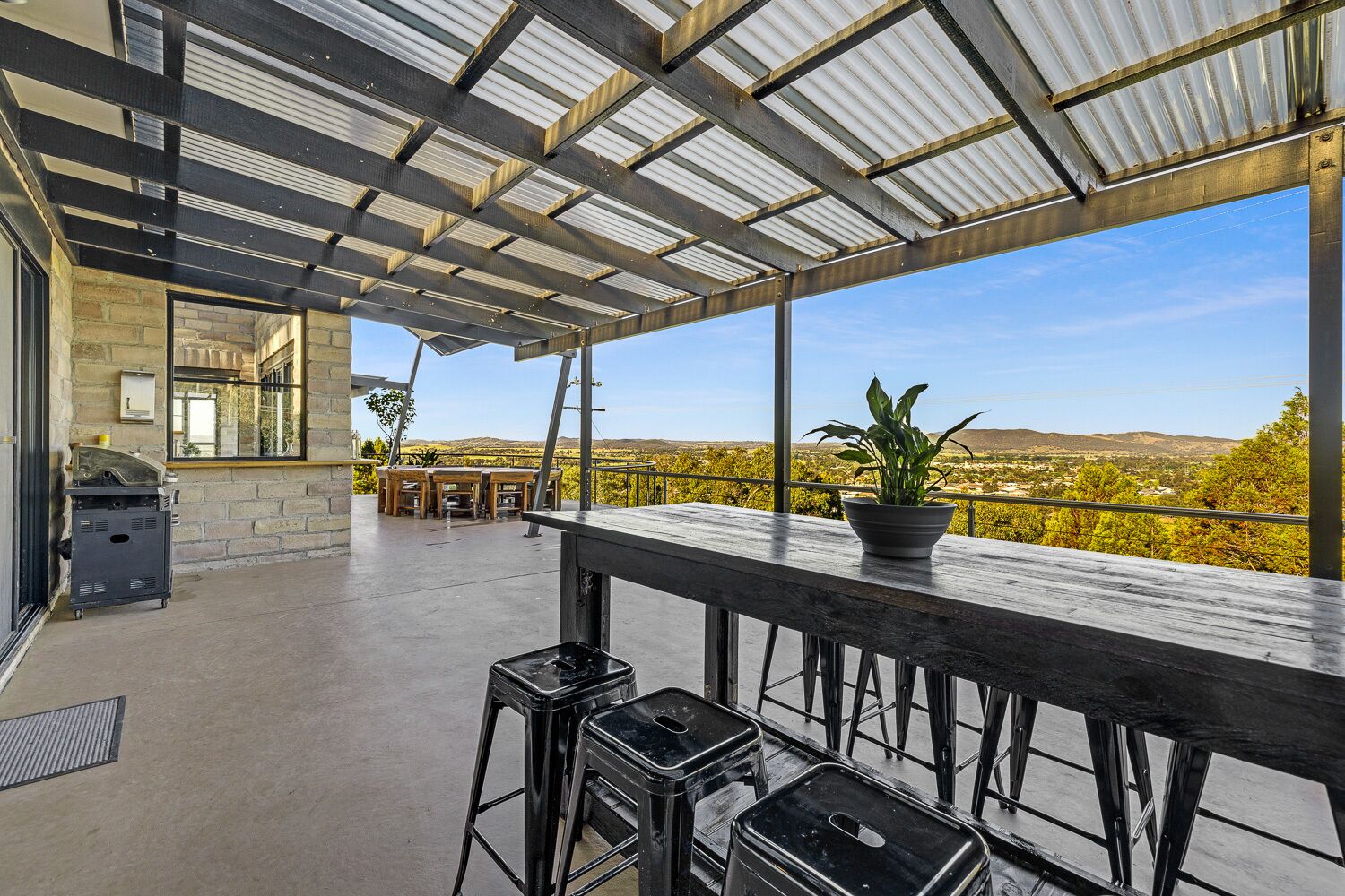 An outdoor patio with a view of a vineyard, a barbecue grill, and a seating area with a potted plant.