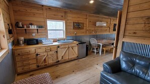 Un intérieur de chalet chaleureux avec des murs en bois, un coin cuisine, un espace repas avec une table et des chaises, et un canapé en cuir.