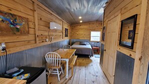 L’intérieur d’une cabane avec une table à manger en bois, des chaises, un banc, un lit et un tableau accroché au mur.