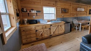 L’intérieur d’un chalet en bois comprend un coin cuisine, des placards en bois, une table à manger et des chaises.