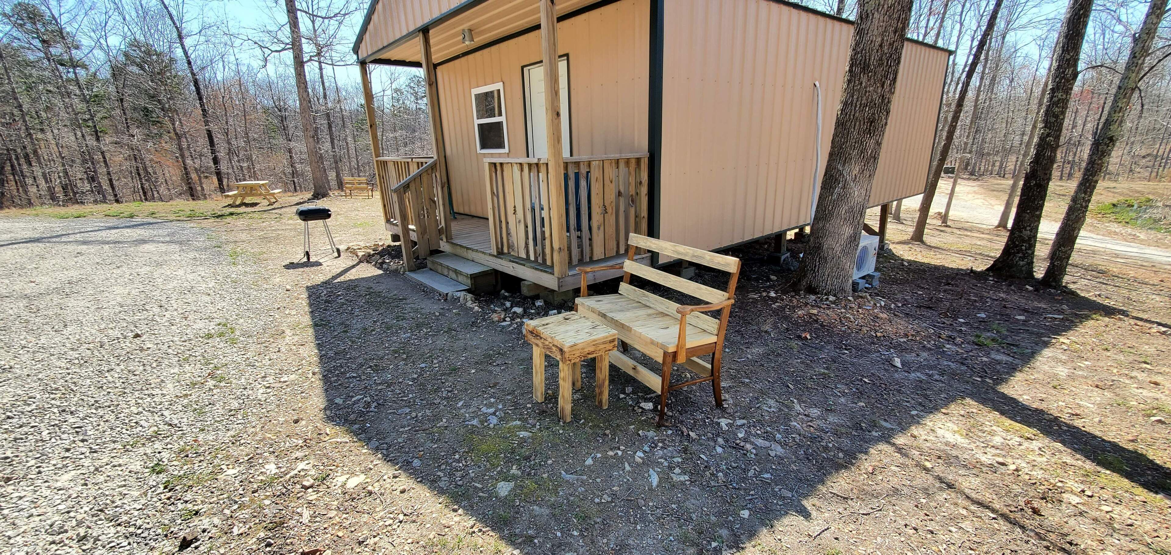 Een klein houten vakantiehuisje met een veranda, een picknicktafel en een bank.