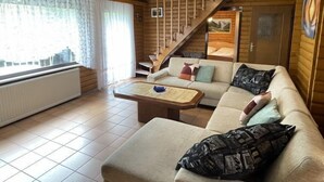 Tunnelmallinen, mökkityylinen huone, jossa on sohva, sohvapöytä ja portaat, jotka johtavat parvelle, jossa on sänky.