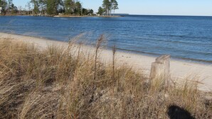 A beach with sand, grass, and a body of water. - Little Bay Waterfront Retreat (White Stone)