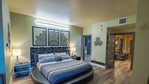 Une chambre à coucher moderne avec un lit aux lignes courbes, une tête de lit aux motifs géométriques et une grande œuvre d’art murale au-dessus du lit.