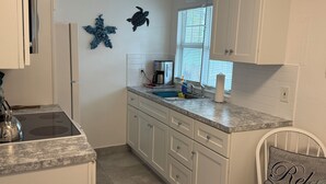 A kitchen with white cabinets, a granite countertop, a coffee maker, and a window with blinds.