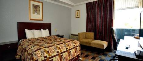 Habitación de hotel con una cama grande, un escritorio, una silla y una ventana con cortinas.