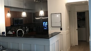 A kitchen with a central island, pendant lights, a whiteboard, and wooden bar stools. - Resort living (Lantana)