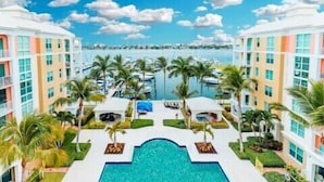 A resort with a central pool surrounded by palm trees and a marina in the background. - Resort living (Lantana)
