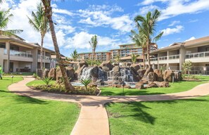 Surrounded by lush greenery and palm trees, this resort features a central water feature and multiple buildings with balconies.