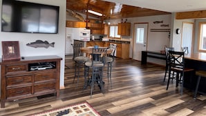 A spacious kitchen with wooden cabinets, a dining area with chairs, a TV mounted on the wall, and a fish decoration.