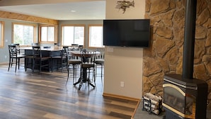 A spacious living area with a stone fireplace, a dining table with chairs, and a flat-screen TV mounted on the wall.
