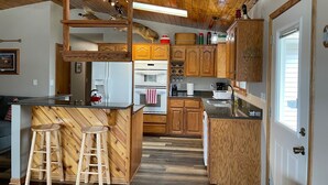 A kitchen with wooden cabinets, a refrigerator, an oven, and a sink. There are two stools and a ladder.