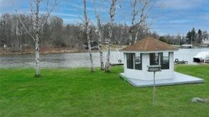 A small, single-story cabin with a sloped roof, situated on a grassy area with trees in the background.