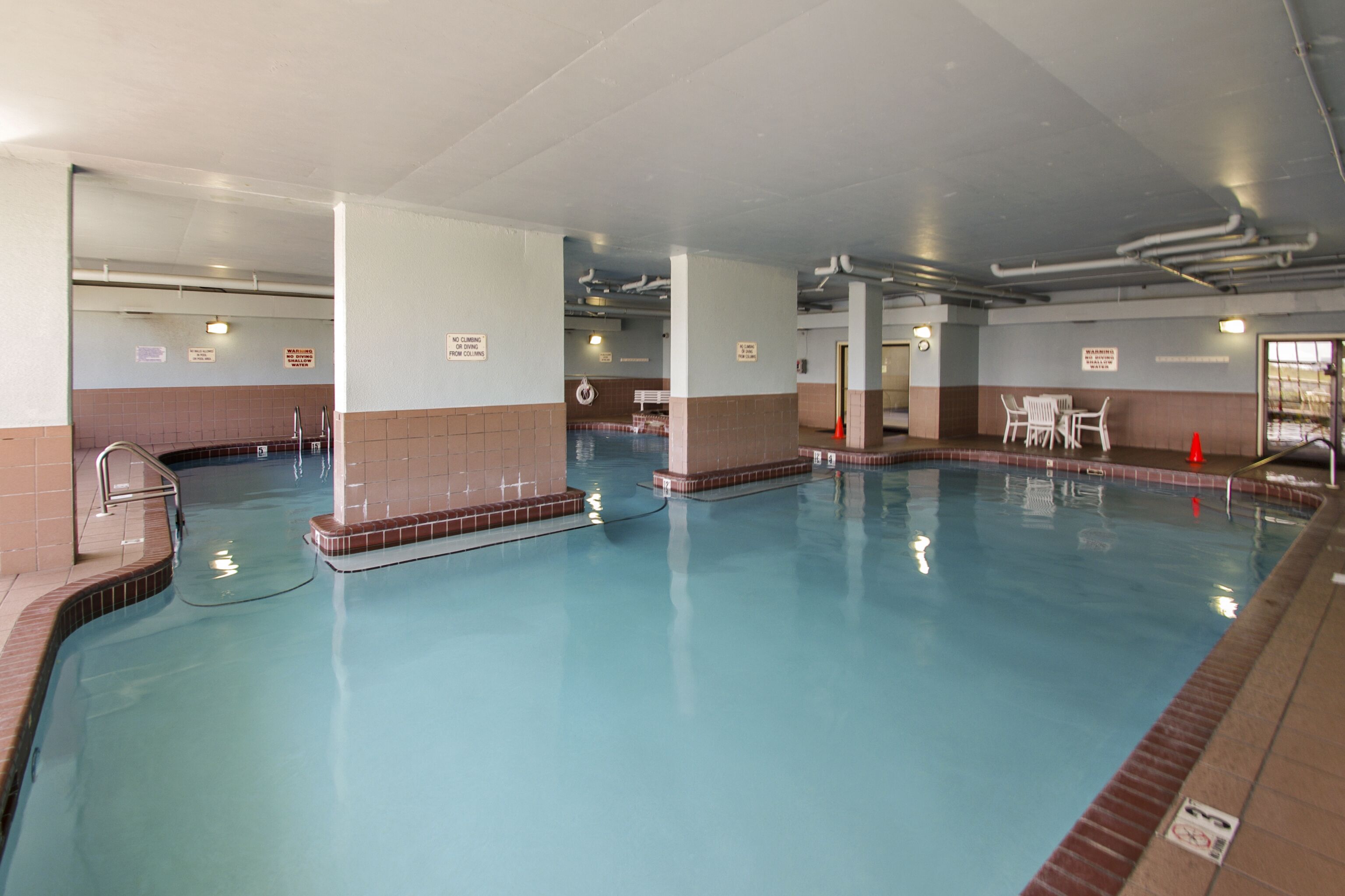 An indoor swimming pool with clear water, tiled walls, and a few chairs around the perimeter.