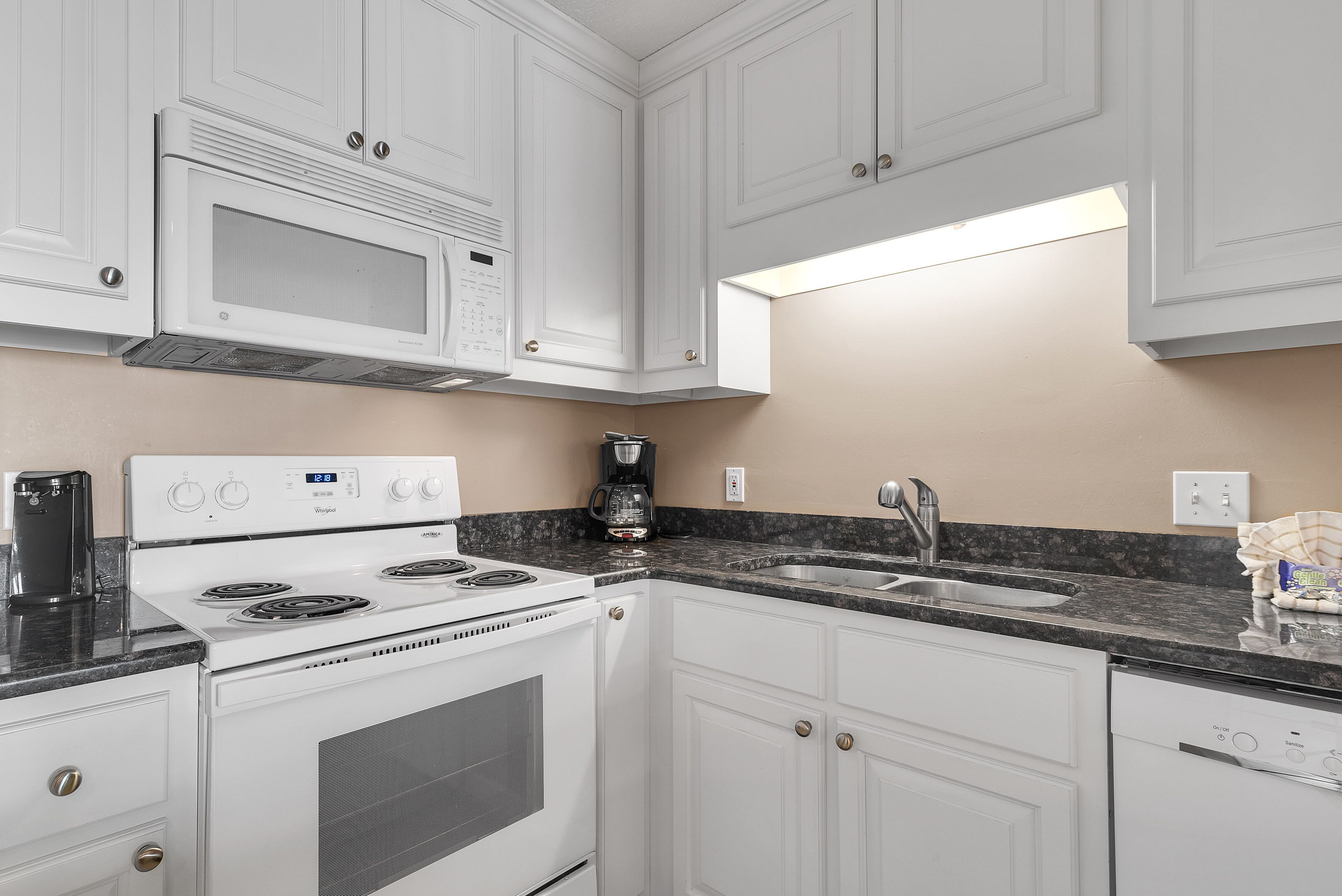 A kitchen with white cabinets, a built-in microwave, a stove, a coffee maker, and a dishwasher.