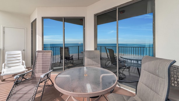 Ein Balkon mit rundem Glastisch und Stühlen, mit Blick auf einen klaren, blauen Himmel und das Meer.