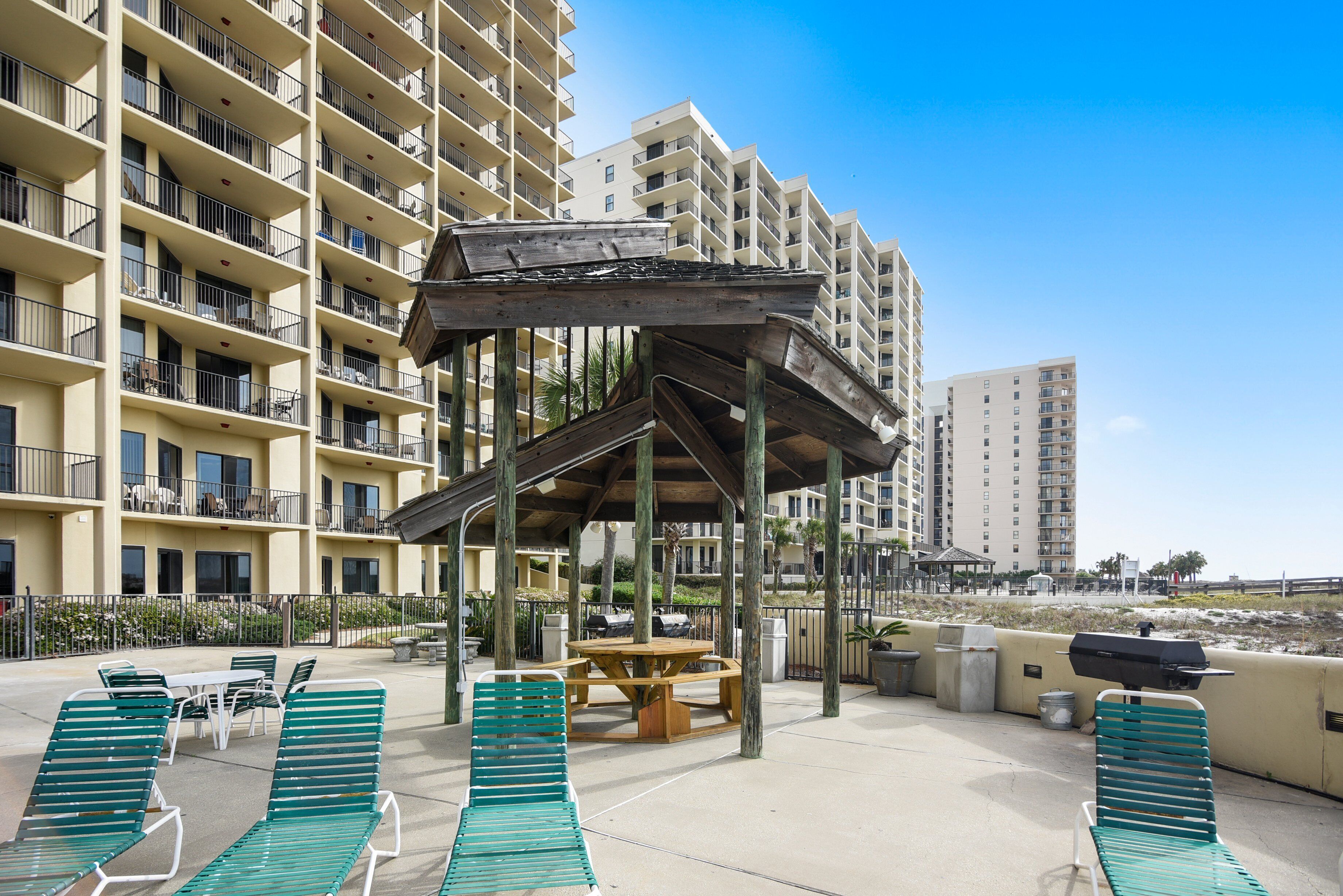 A rooftop patio with green lounge chairs, a wooden table, and a barbecue grill.